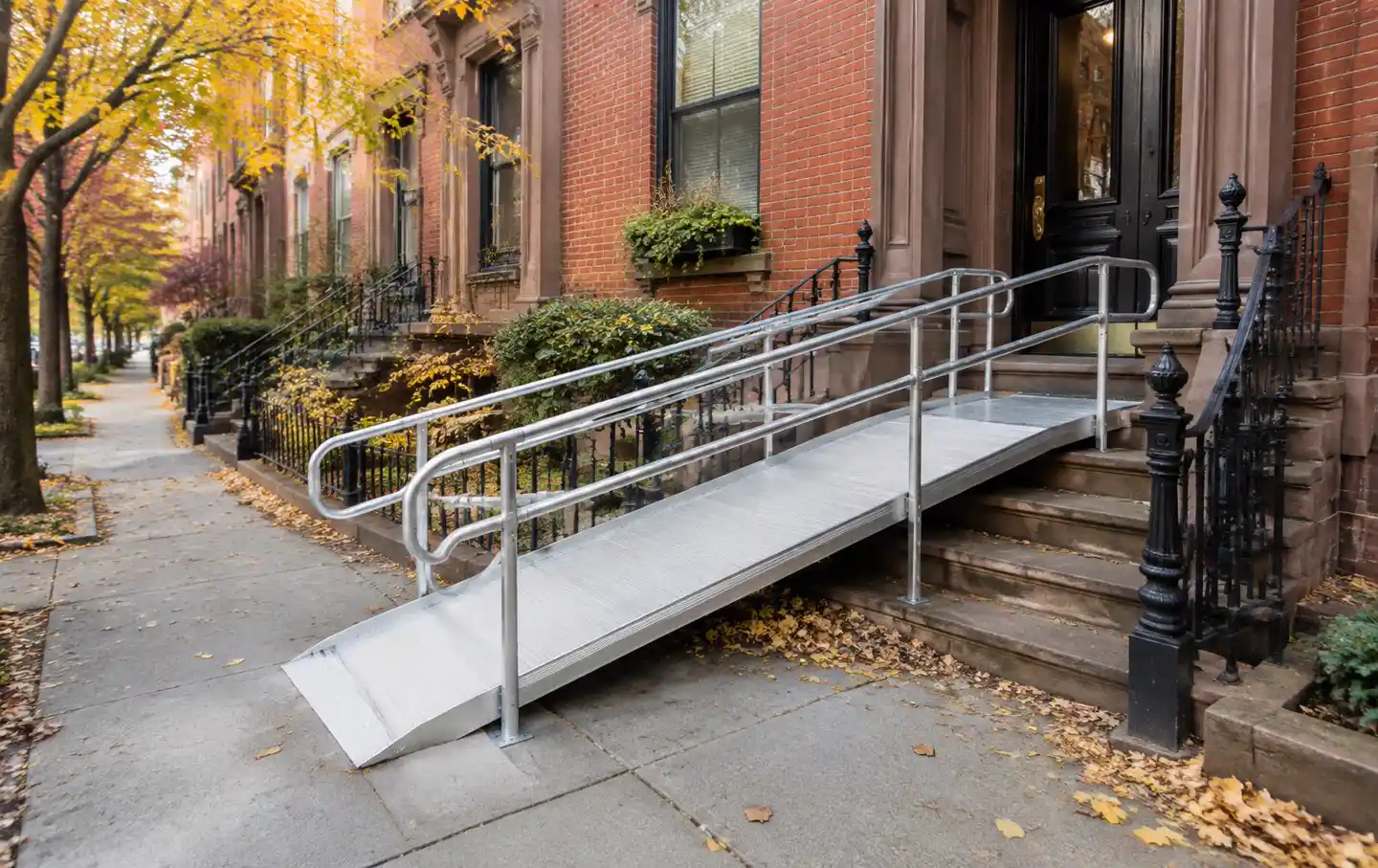 Modular aluminum wheelchair ramp with handrails leading to the entrance of a Boston brick row house