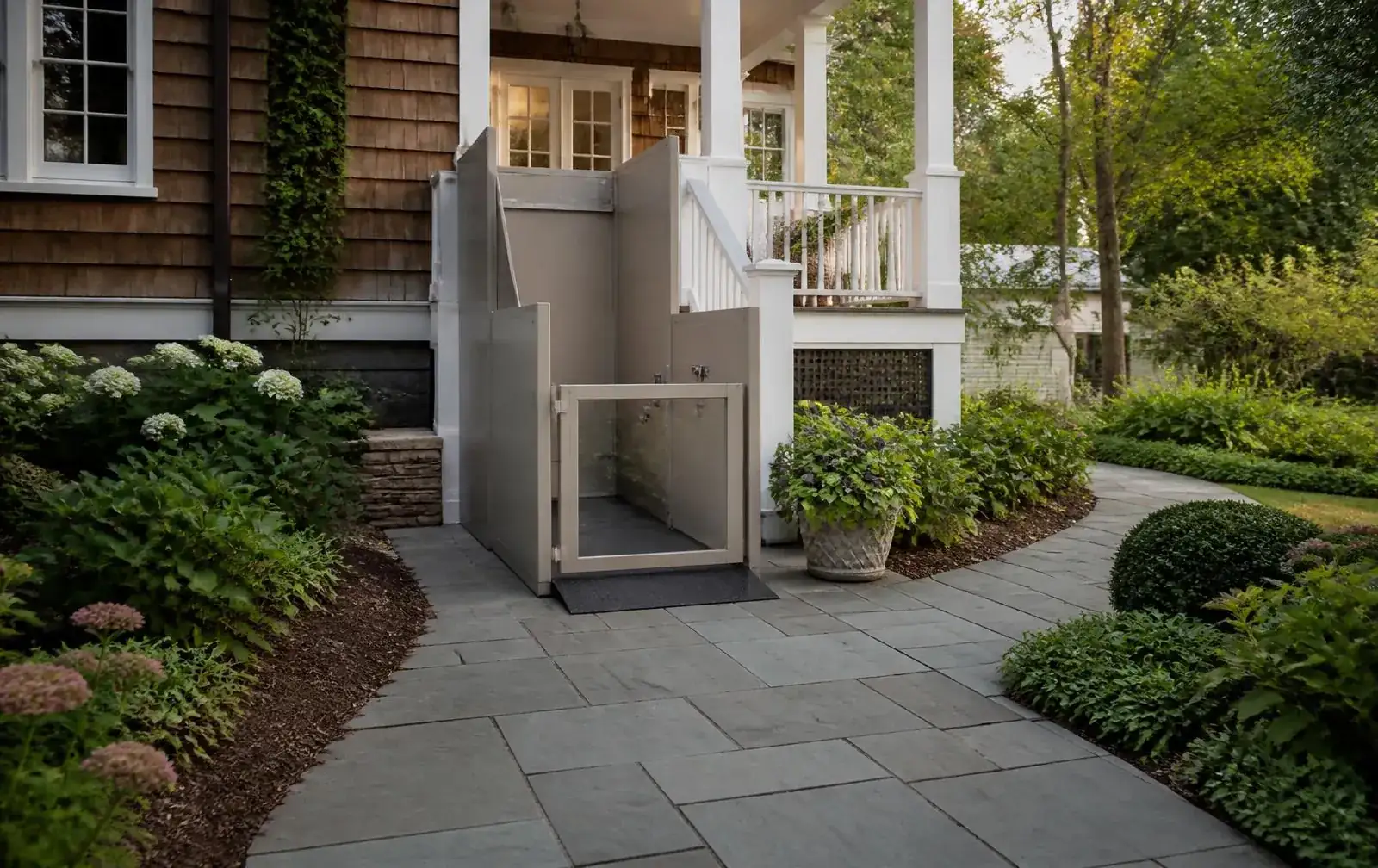 Vertical platform lift integrated beside the porch of a shingle-style Newton home