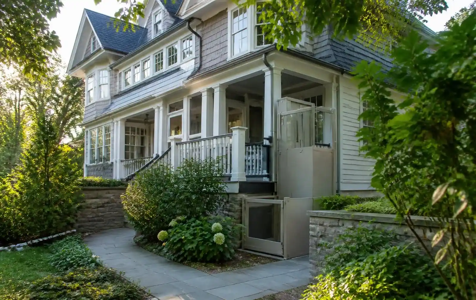 Vertical platform lift integrated beside the porch of a leafy Waban home