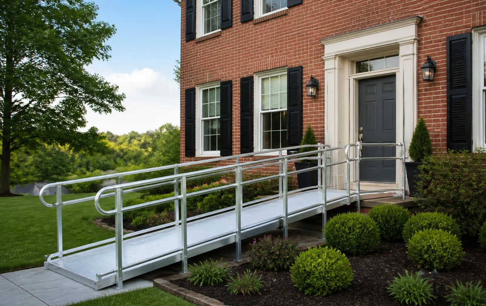 Modular aluminum wheelchair ramp with handrails at the front entrance of a brick colonial home