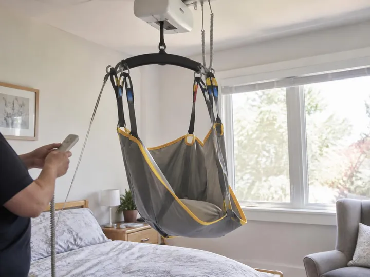 Caregiver holding a ceiling lift hand control beside a sling hanging from the motor