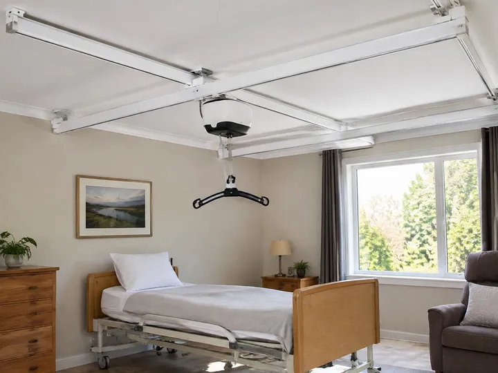 Ceiling lift on an X-Y gantry track spanning a bedroom ceiling above a care bed