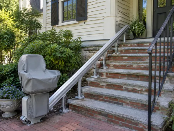 Outdoor stairlift with a weather cover on an aluminum rail beside brick and granite exterior steps