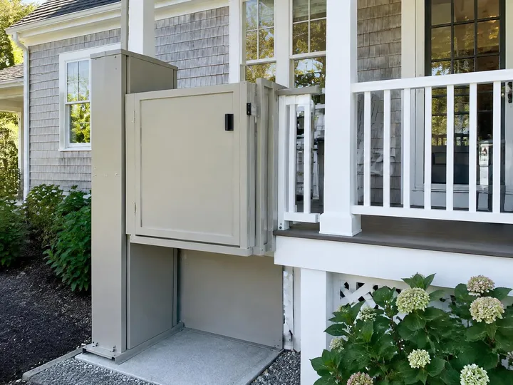 Enclosed porch lift with a gated platform raised beside a painted wood porch