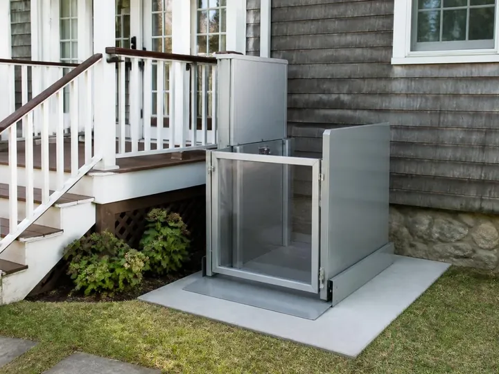 Vertical platform lift with a steel gate installed beside a porch deck on a concrete pad